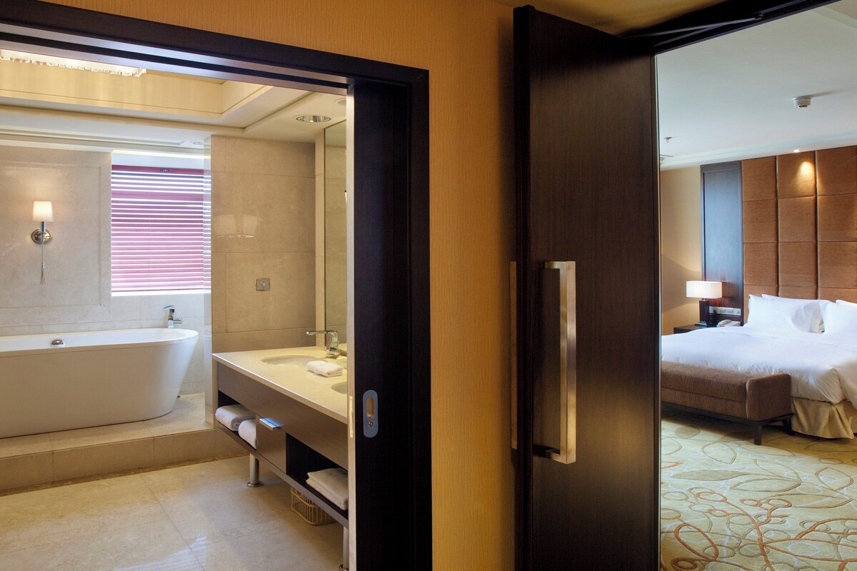 A hotel bathroom with a freestanding bathtub, a vanity with a mirror, and a shower area.