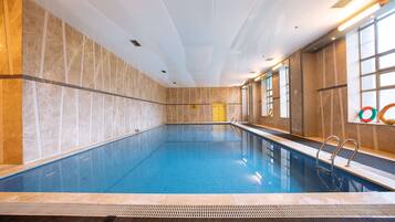An indoor swimming pool with clear blue water, tiled walls, and a tiled floor. There are two doors, one yellow and one white, and a window on the right side.