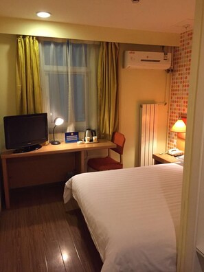 A hotel room with a bed, a desk with a computer, a chair, a TV, a lamp, and an air conditioning unit. - Home Inn (Beijing)