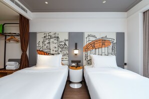 Een hotelkamer met twee bedden, een nachtkastje met een lamp, een aan de muur hangend kunstwerk en een kapstok.