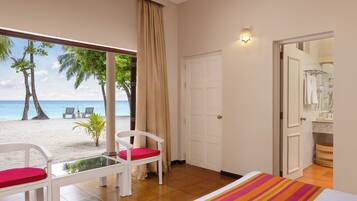 Une chambre d’hôtel avec vue sur la plage, un lit, une fenêtre avec des rideaux, une porte blanche et une salle de bain visible à travers une porte ouverte.