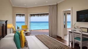 A hotel room with a bed, a desk, a chair, a TV, and a view of the ocean.