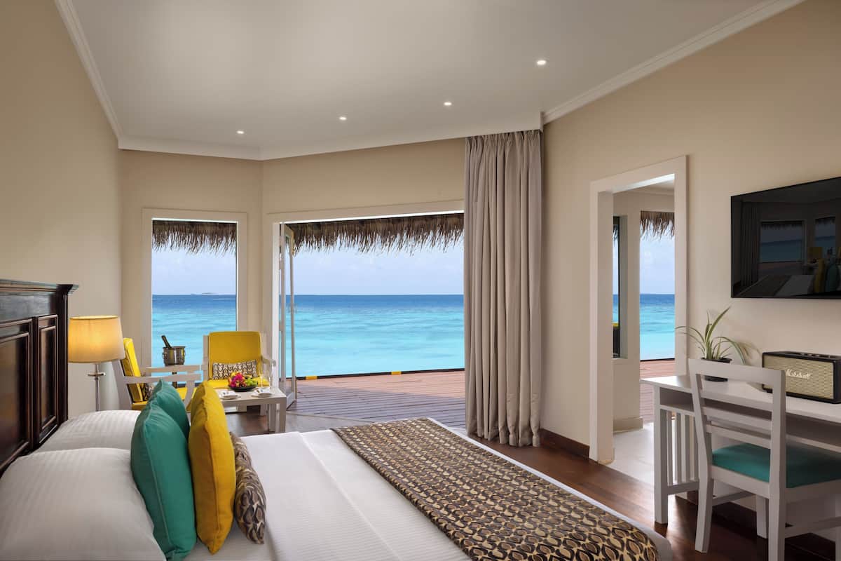 A hotel room with a bed, a desk, a chair, a TV, and a view of the ocean.