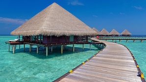 Overwater bungalows with thatched roofs connected by wooden walkways over clear turquoise water.
