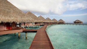 Overwater bungalows with thatched roofs connected by wooden walkways over clear turquoise water.