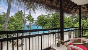 A balcony with a view of the beach and ocean, a table with chairs, and a potted plant.