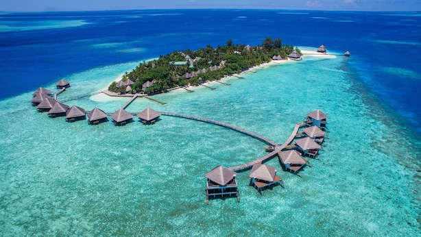 An aerial view of an overwater resort with thatched-roof bungalows connected by a wooden walkway.