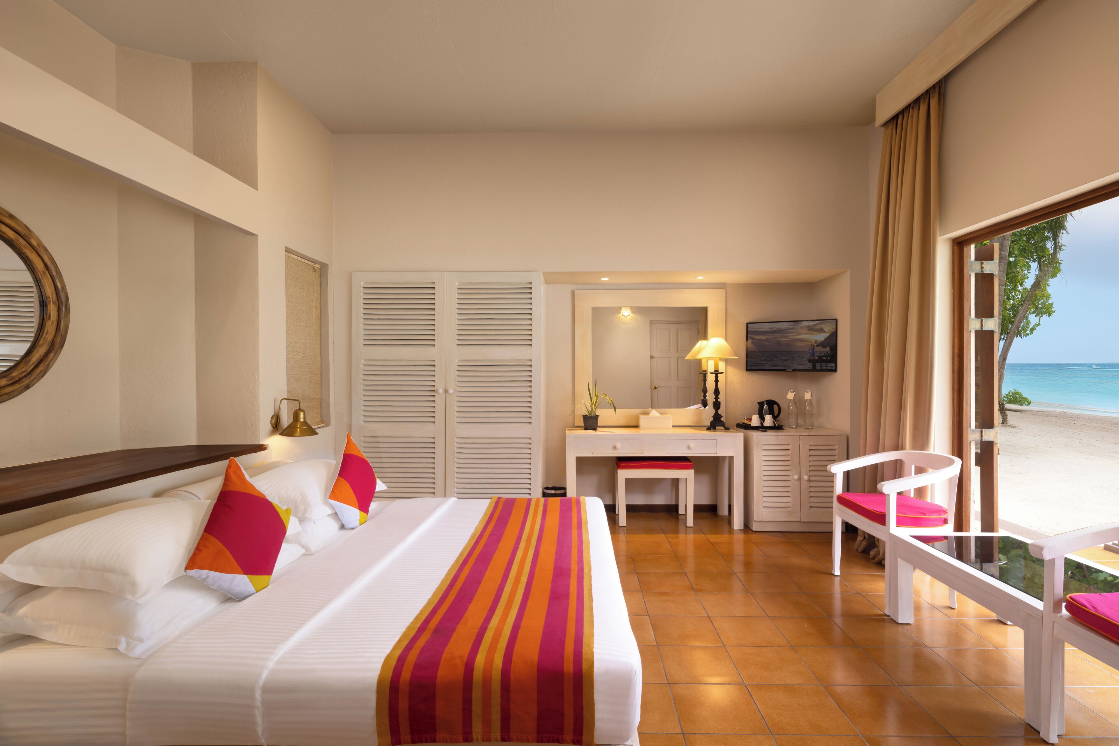 A hotel room with a bed, desk, chair, and a view of the beach.