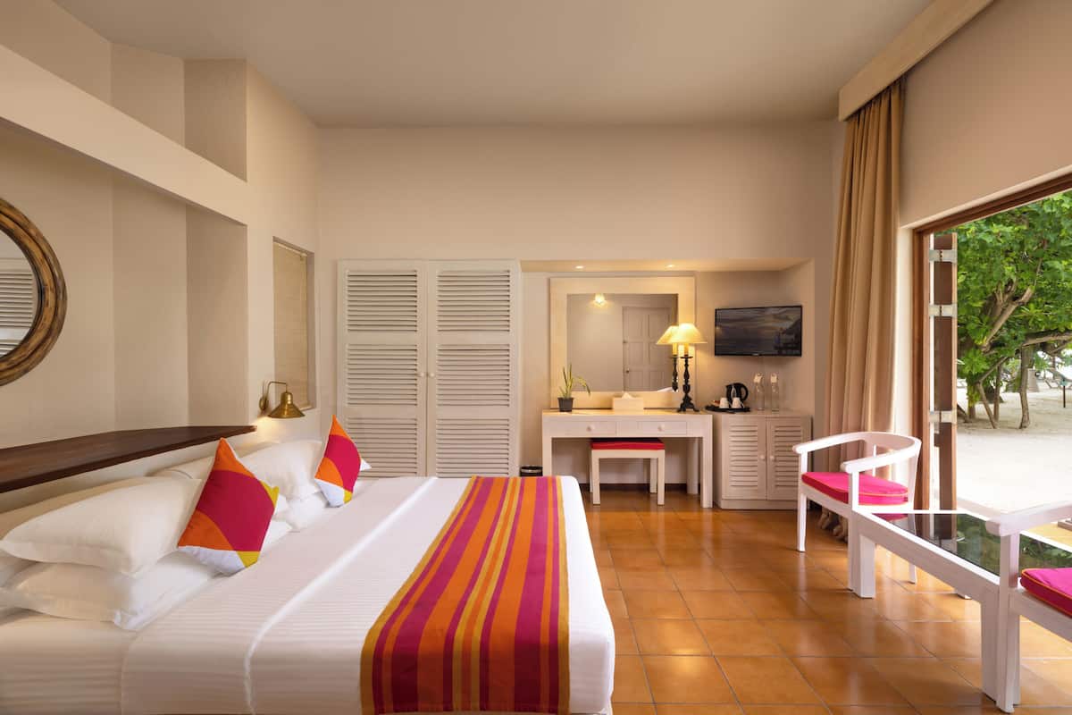 A hotel room with a bed, a desk, a chair, a TV, and a window with a view of trees.