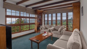 A spacious living room with a large window, a wooden coffee table, a beige sofa, and a bookshelf. - Heritance Tea Factory (Kandapola)