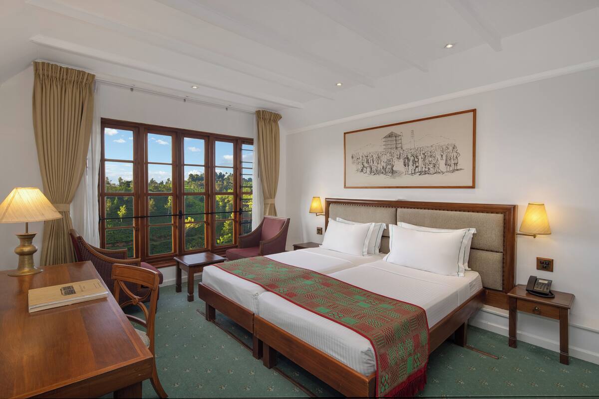 A hotel room with a large bed, a desk, a chair, a nightstand, and a window with curtains.