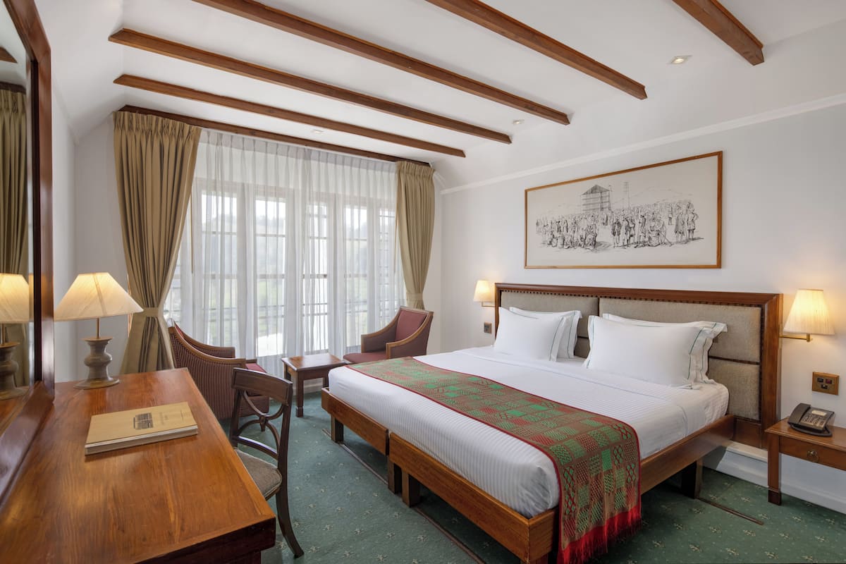 A hotel room with a wooden bed, a desk with a lamp, a chair, and a framed picture on the wall.