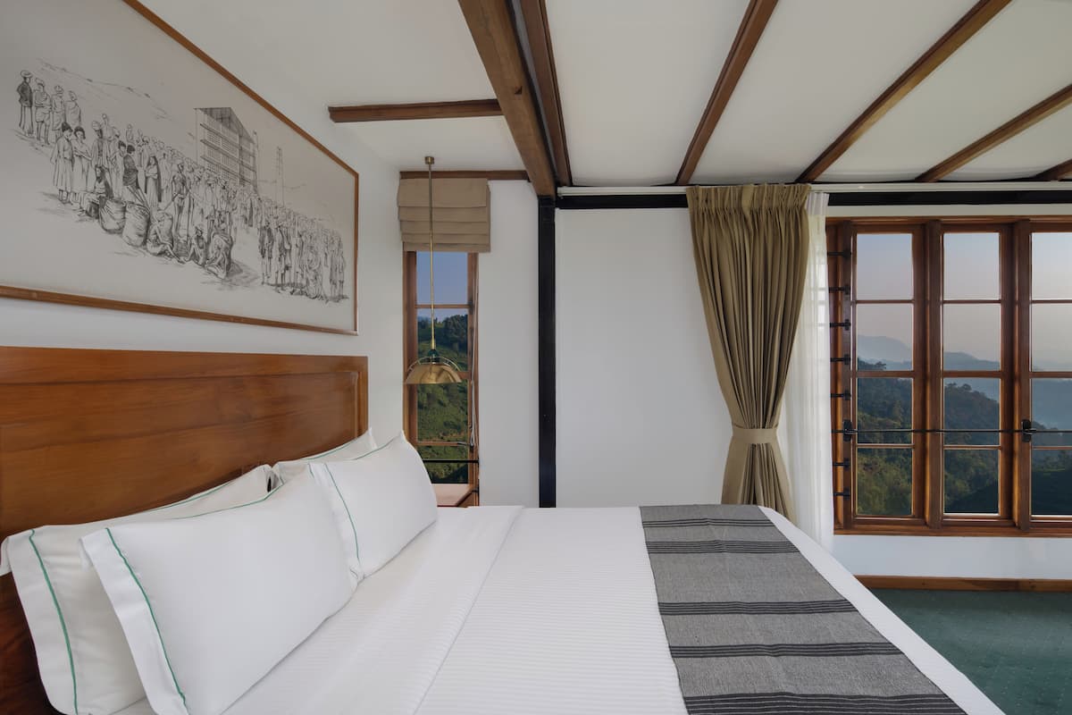 A bedroom with a large bed, a view of the outdoors through a window, and a painting on the wall.