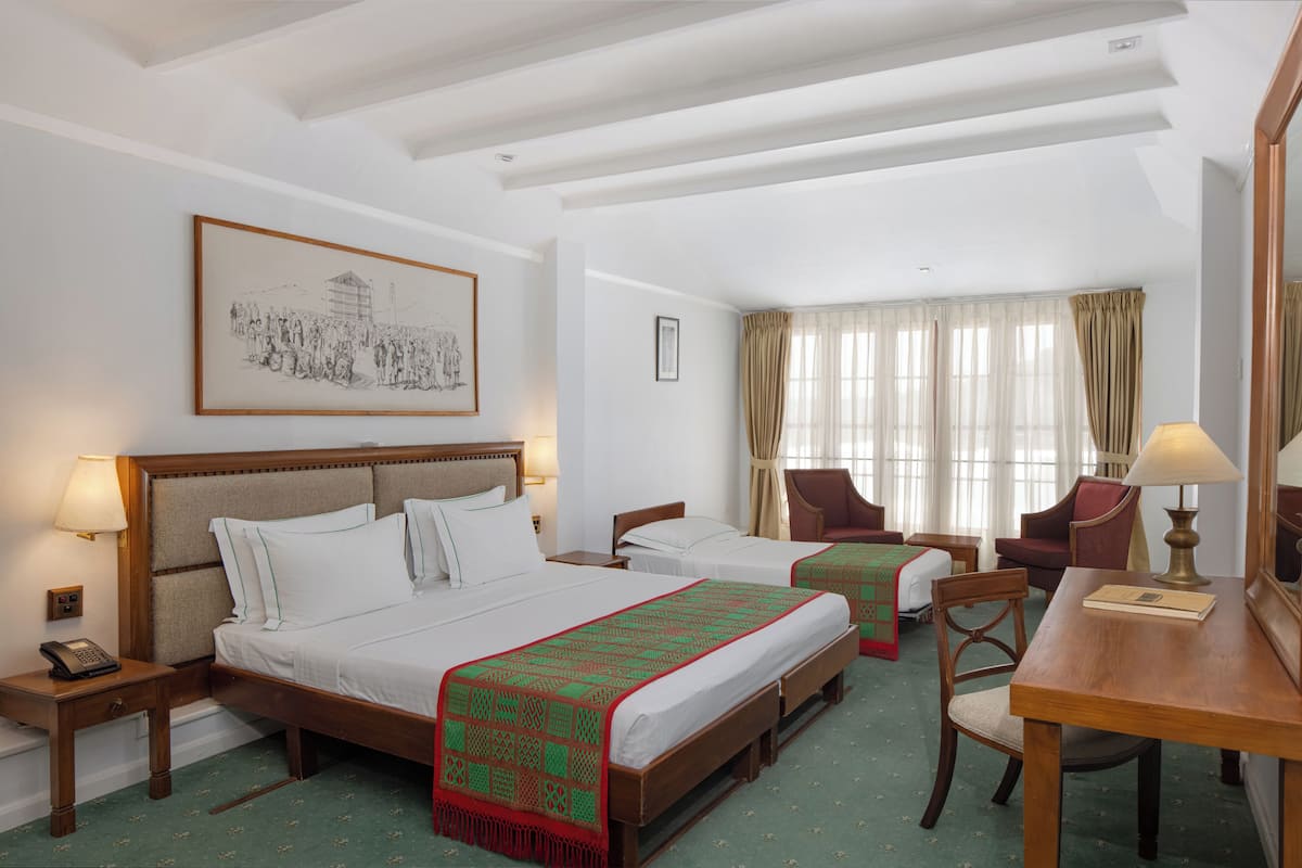 A hotel room with two beds, a desk, chairs, a telephone, and a framed picture on the wall.