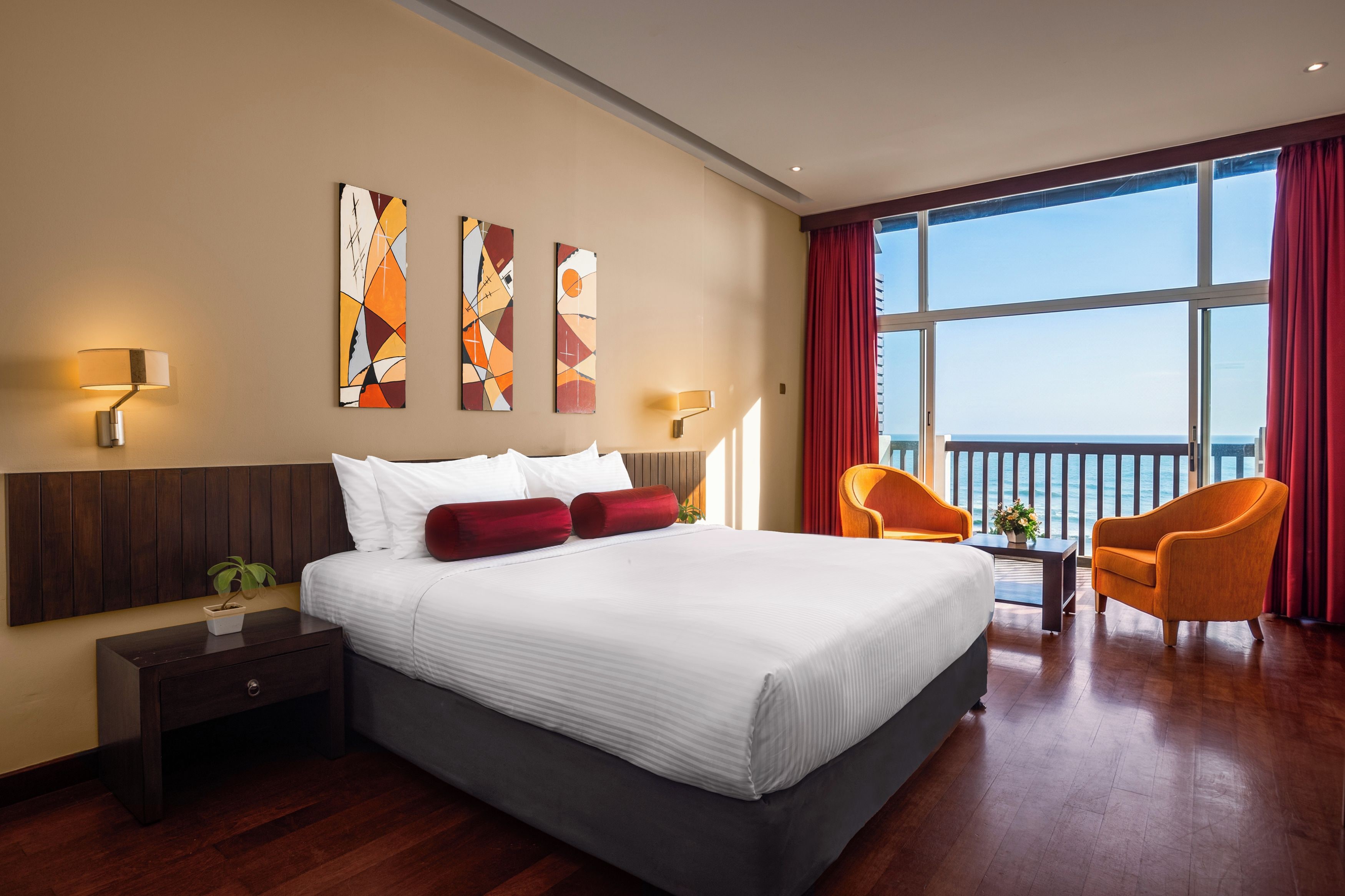 A hotel room with a large bed, two chairs, a nightstand, and artwork on the wall.