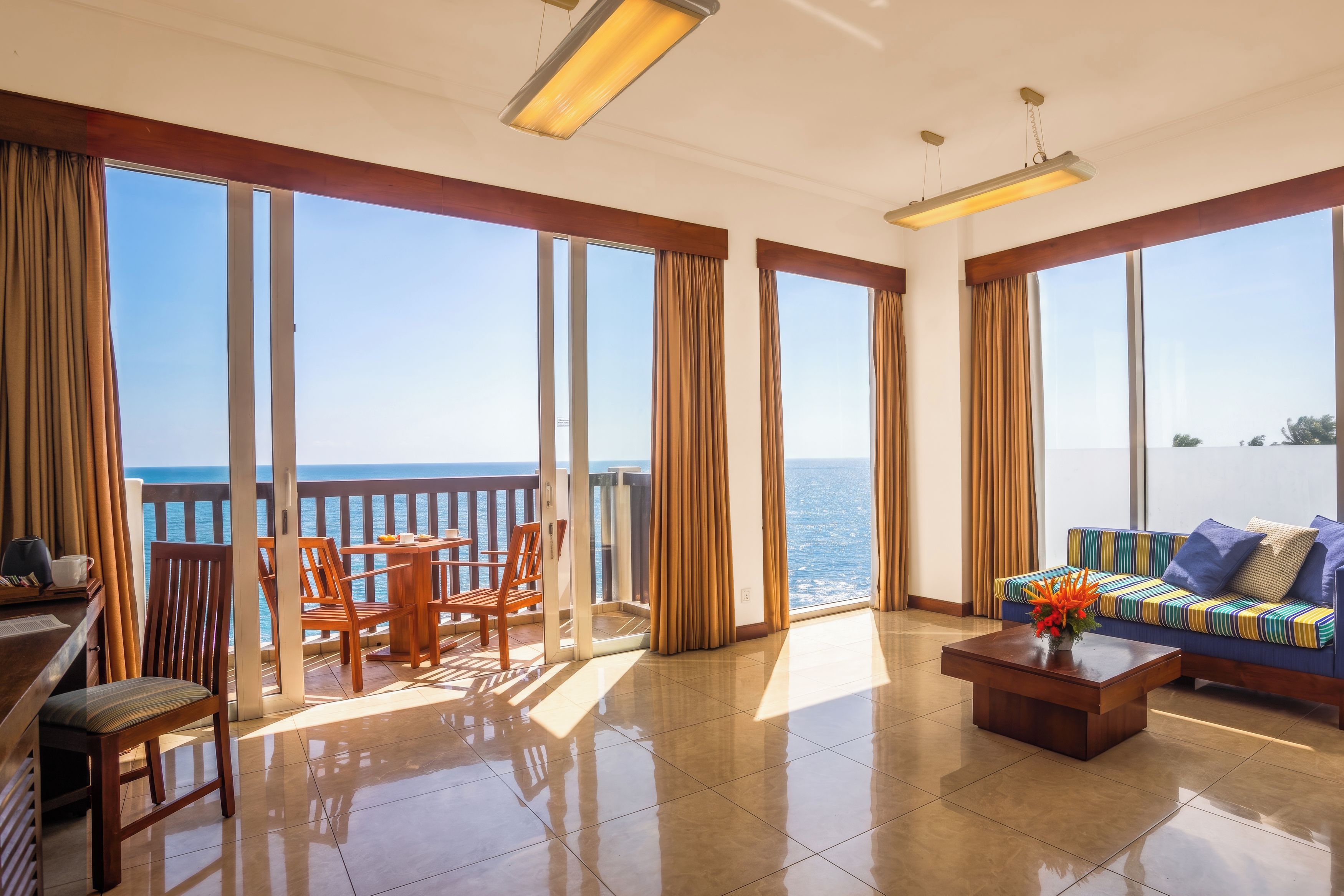 Amplia sala de estar con balcón con vistas al mar, amueblada con un sofá, una mesa de centro y sillas.