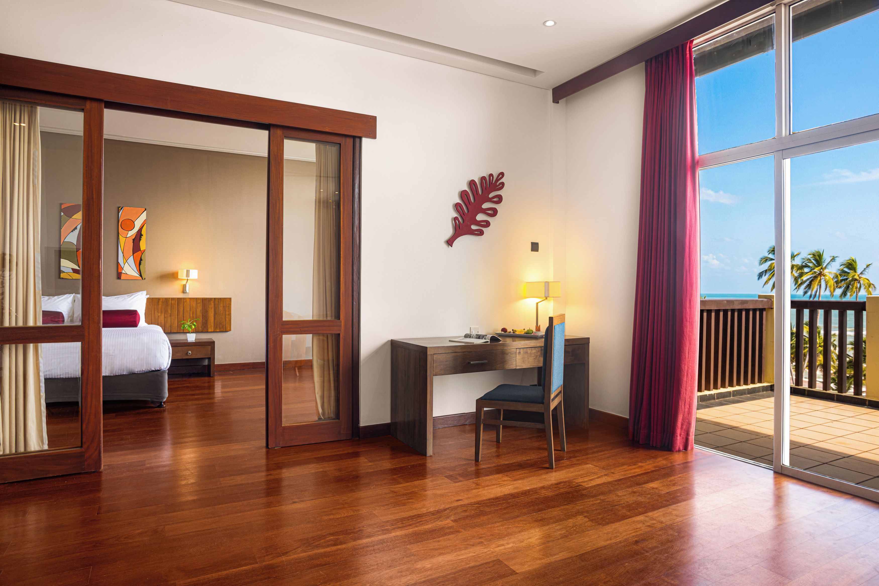 A hotel room with a bed, desk, chair, and a view of the ocean.