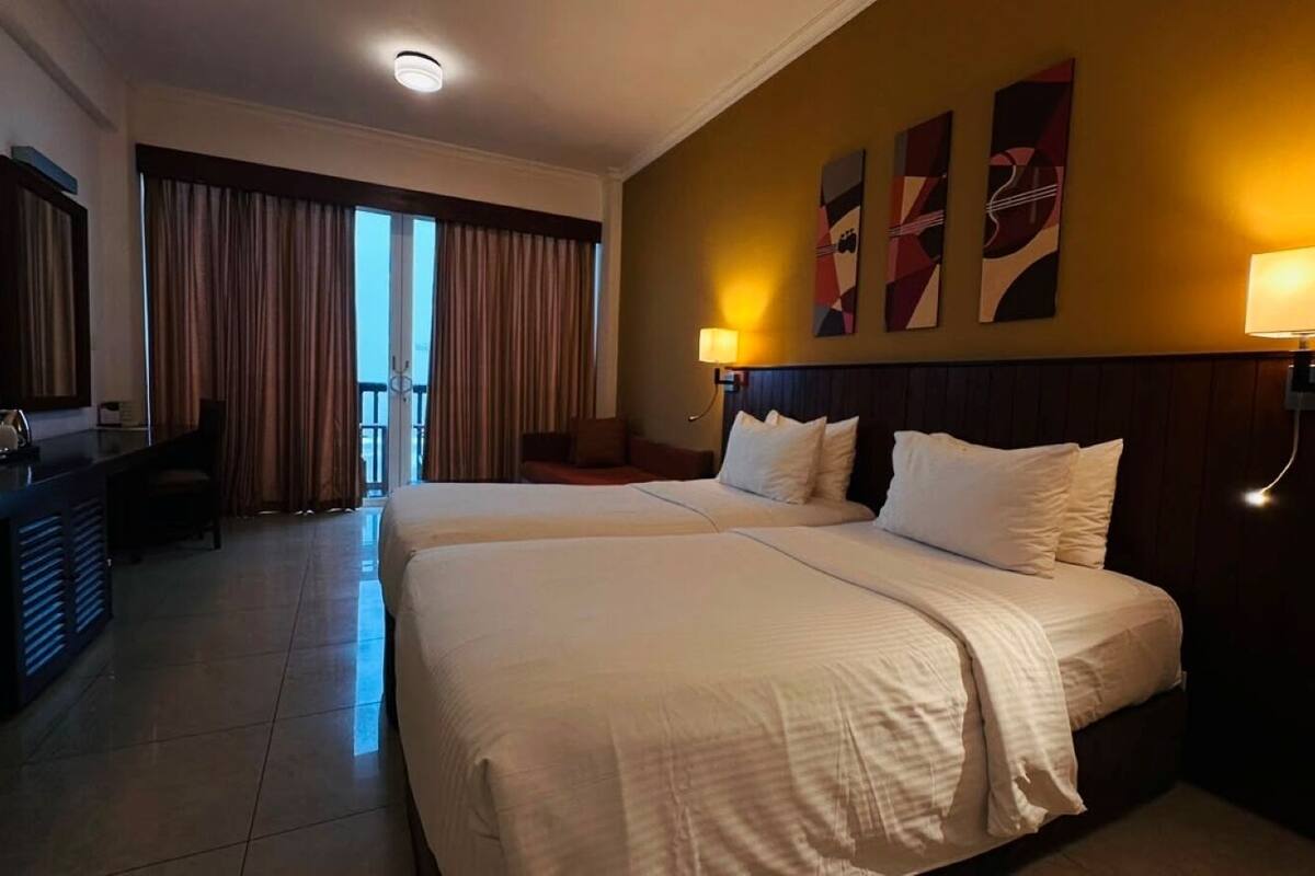 Quarto de hotel com duas camas, uma escrivaninha e vista para o exterior.