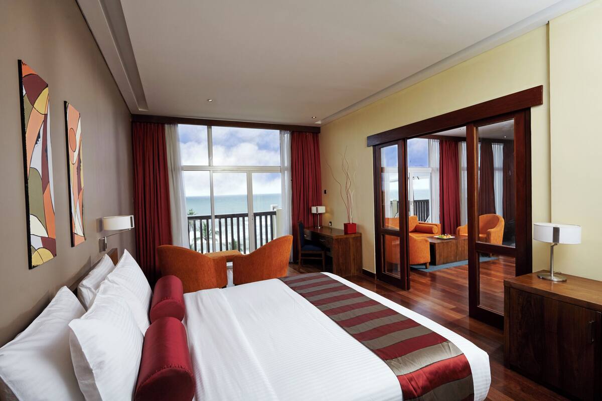 Quarto de hotel com uma cama grande, uma escrivaninha, uma cadeira e vista para o mar.