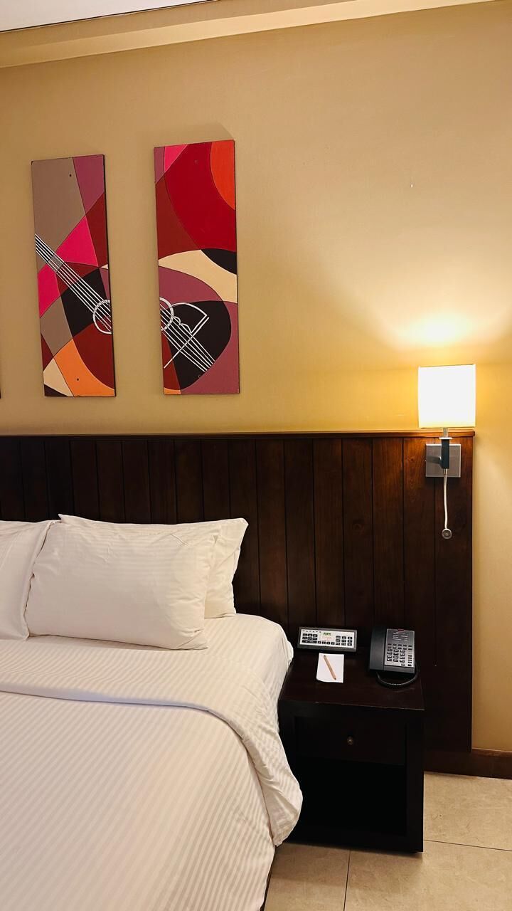 Una habitación de hotel con una cama, una mesita de noche con un teléfono y dos cuadros abstractos en la pared.