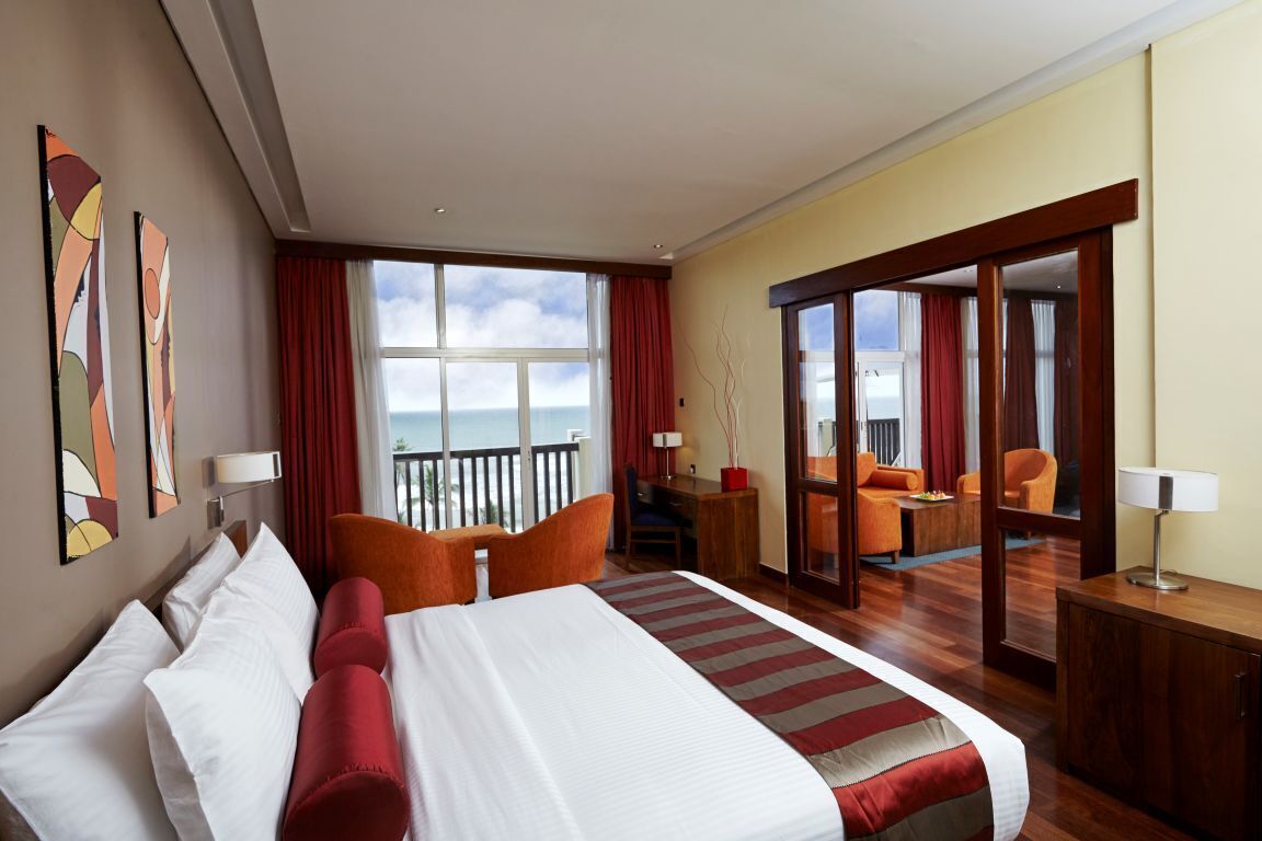 Habitación de hotel con una cama grande, un escritorio, una silla, un sofá y un balcón con vista al mar.
