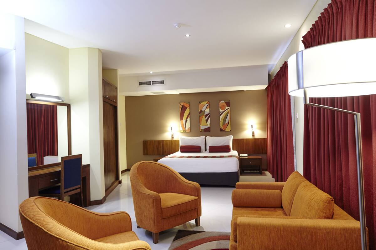 Quarto de hotel com cama, duas poltronas, uma mesa e uma luminária.
