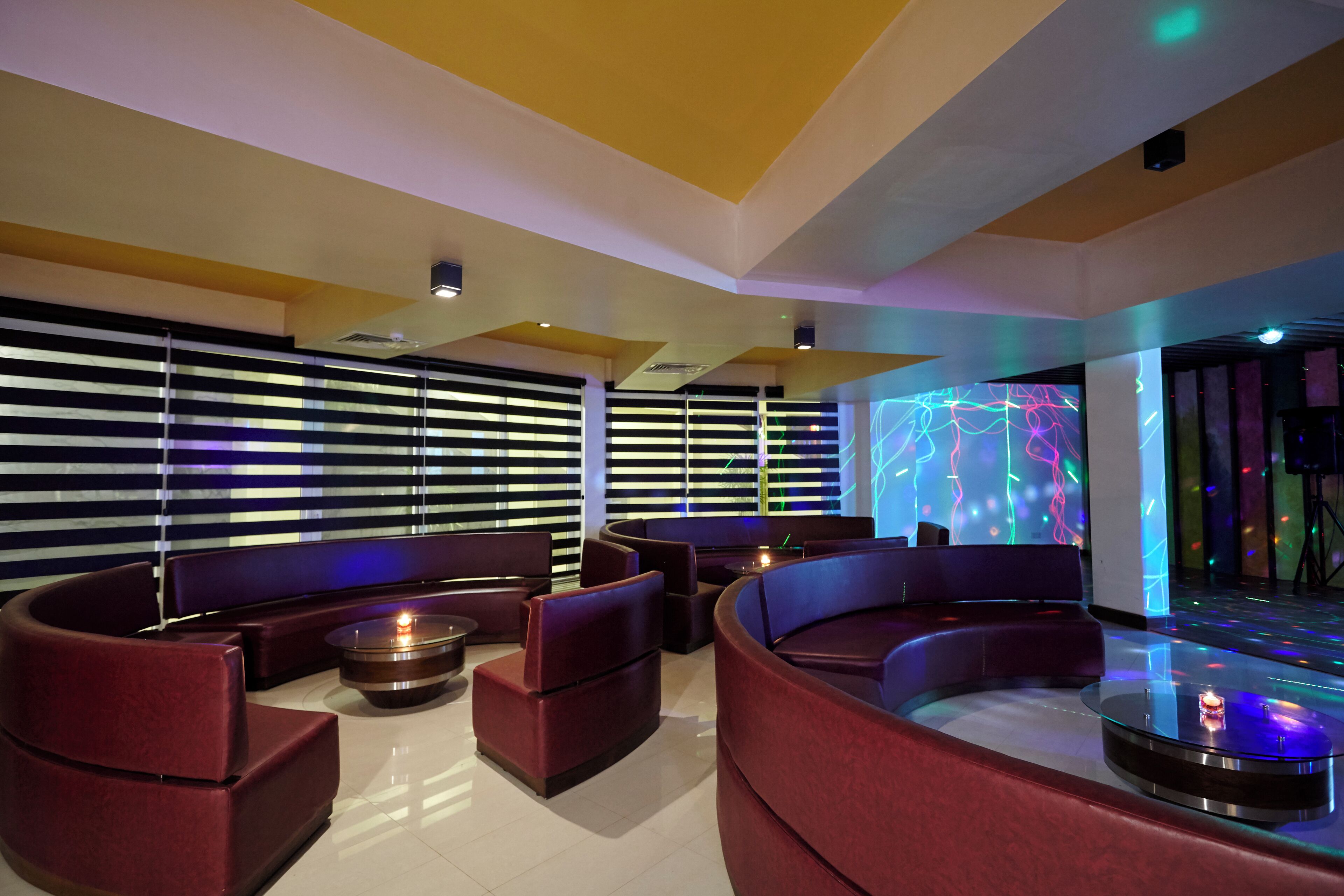 Un área de estar moderna con asientos curvos, una mesa central con vela y una pared con patrones de luz de colores.