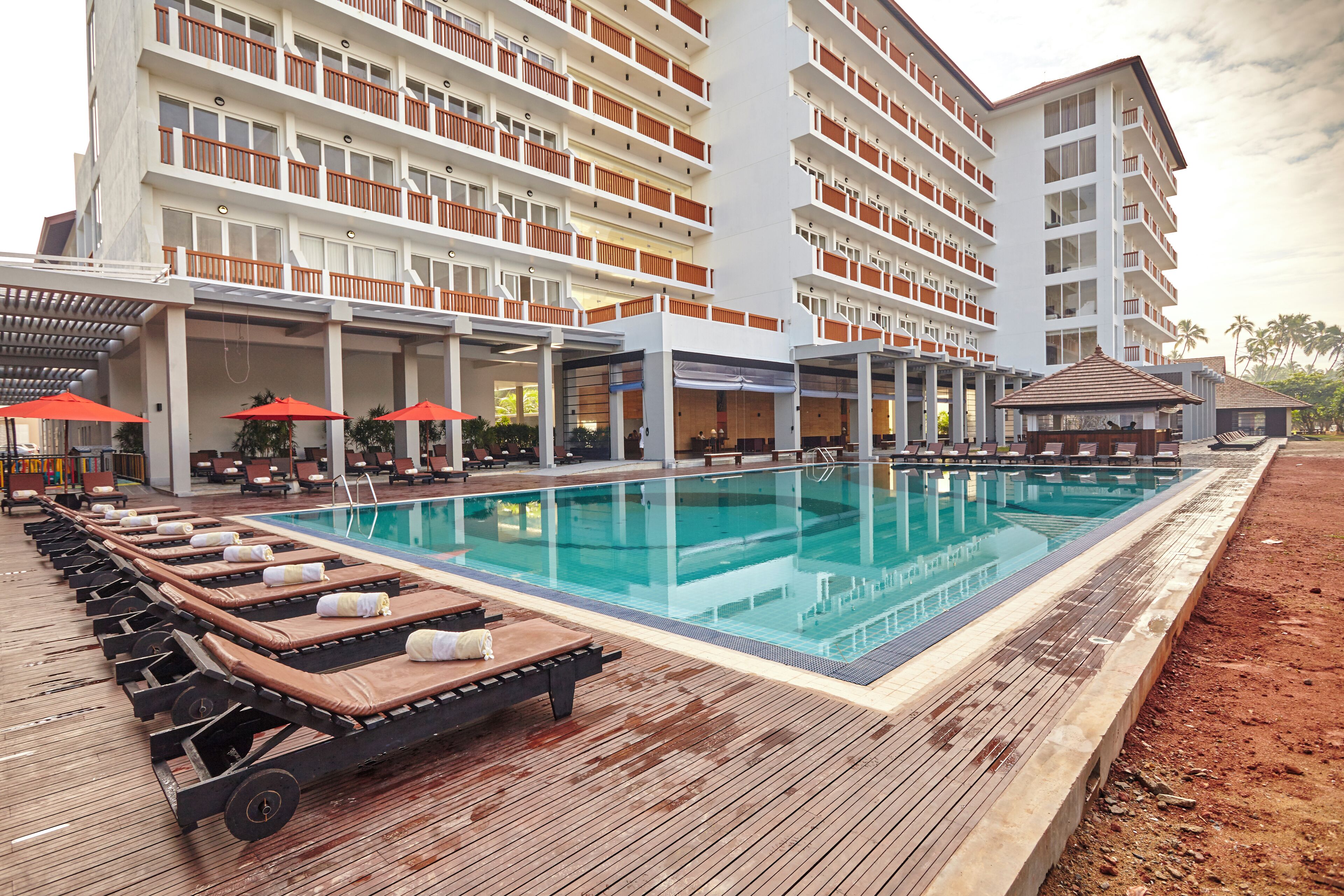 A hotel with a swimming pool, sun loungers, and a covered area with umbrellas.