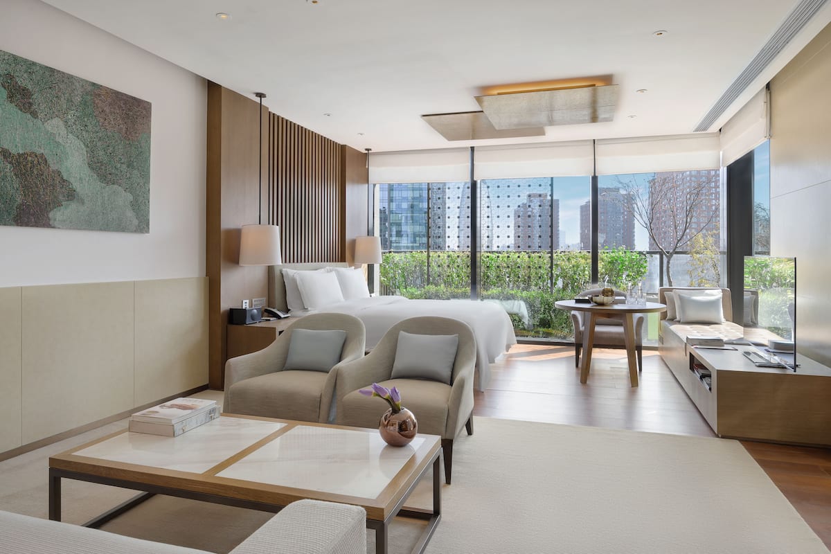 A modern hotel room with a large bed, two armchairs, a coffee table, and a dining area.