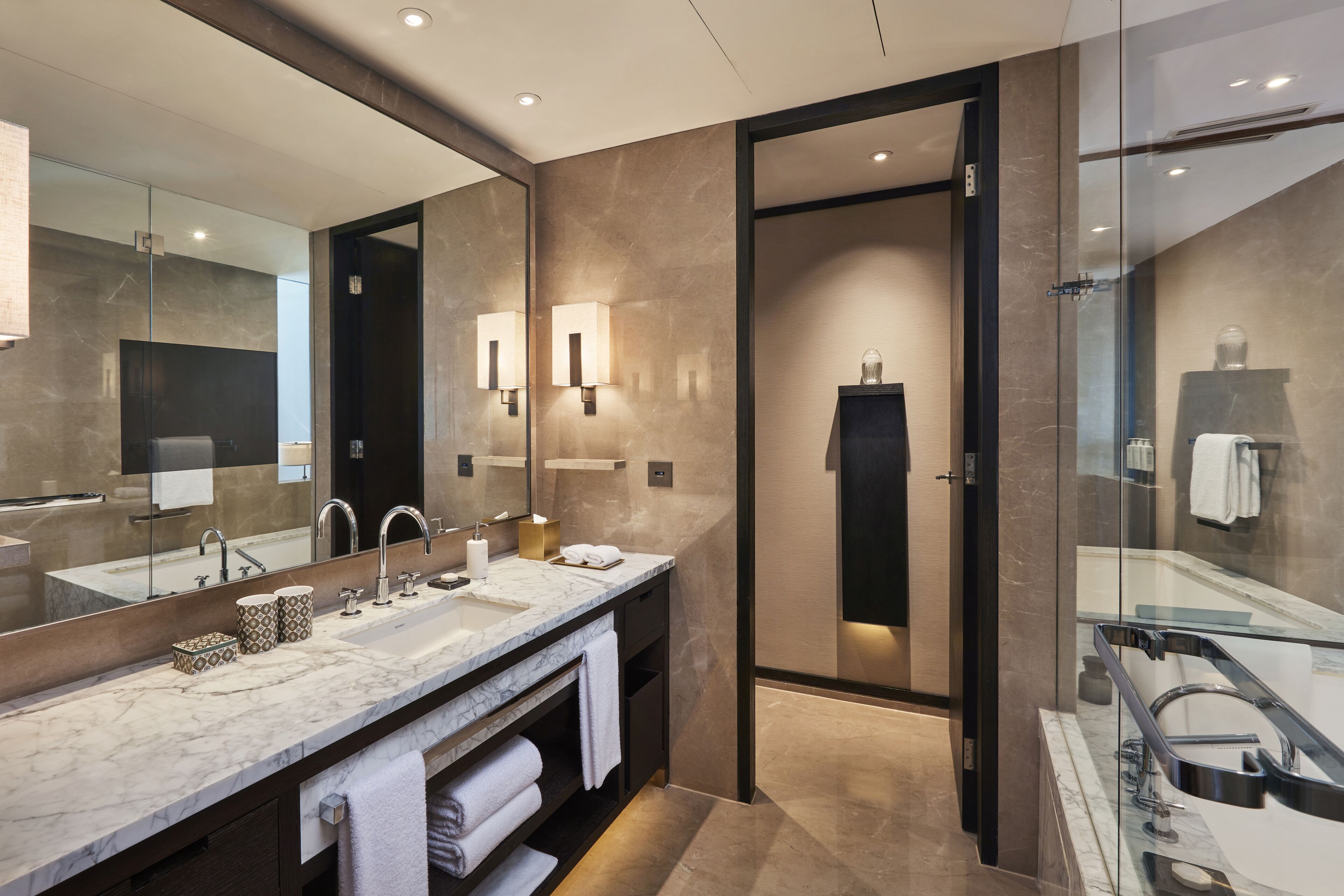 Un baño moderno con un espejo grande, lavamanos dobles y una zona de ducha con paredes de vidrio.