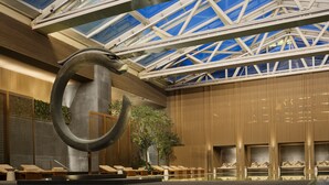 A modern indoor pool area with lounge chairs, a large abstract sculpture, and a high ceiling with skylights. - Rosewood Beijing (Beijing)