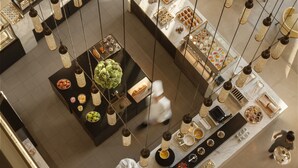 A high-ceilinged restaurant with hanging light fixtures, a central serving area, and multiple seating options. - Rosewood Beijing (Beijing)
