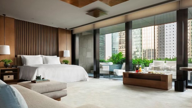 A modern hotel room with a large bed, a sofa, a coffee table, and a view of the city through large windows. - Rosewood Beijing (Beijing)