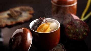 A traditional tea set with a teapot and cups, a piece of bread, and a fruit.