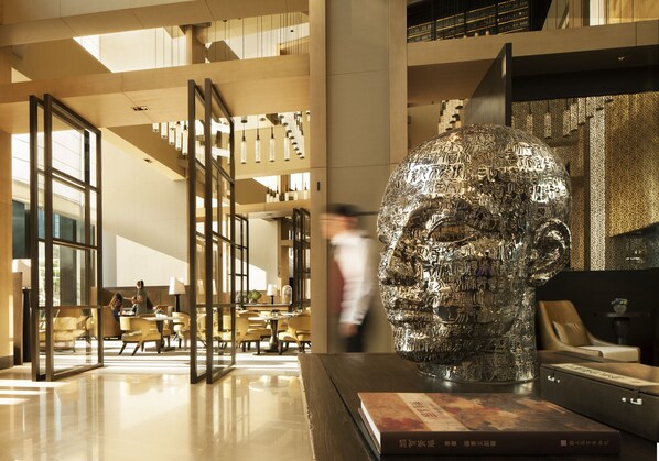 A modern interior with a large metallic sculpture, a well-lit lobby, and a seating area with tables and chairs. - Rosewood Beijing (Beijing)