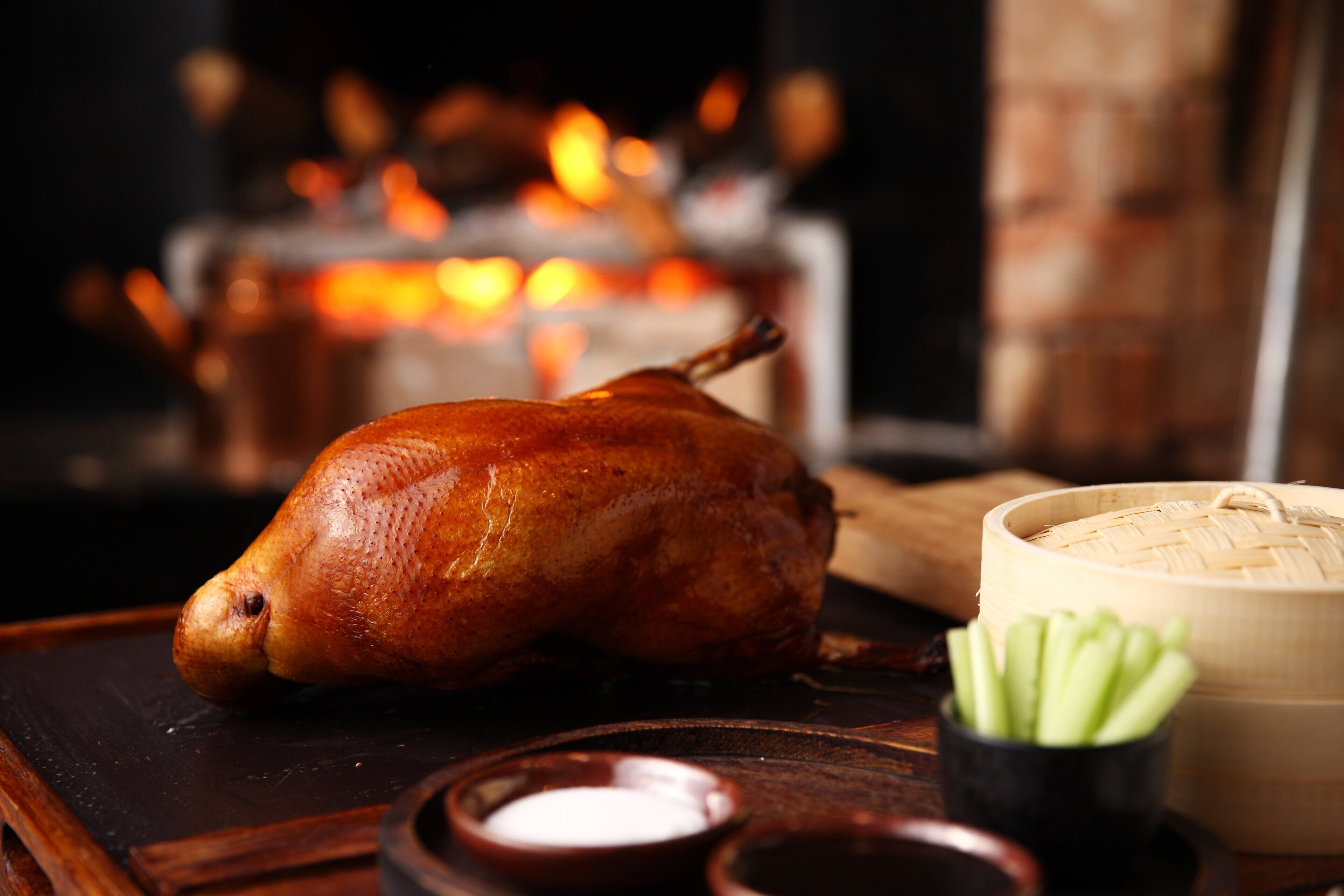 Un pato asado sobre una bandeja de madera, con un tazón de sopa y un recipiente pequeño de salsa.