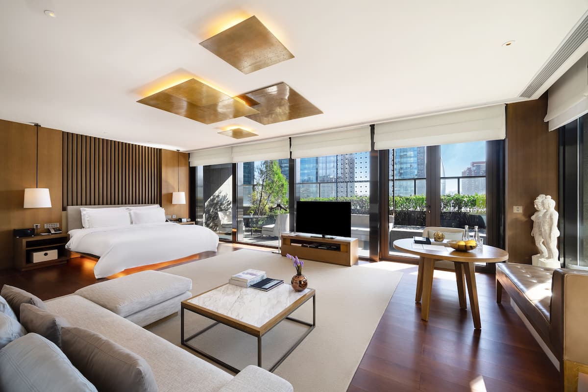 A modern hotel room with a large bed, a TV, a sofa, a coffee table, and a statue.