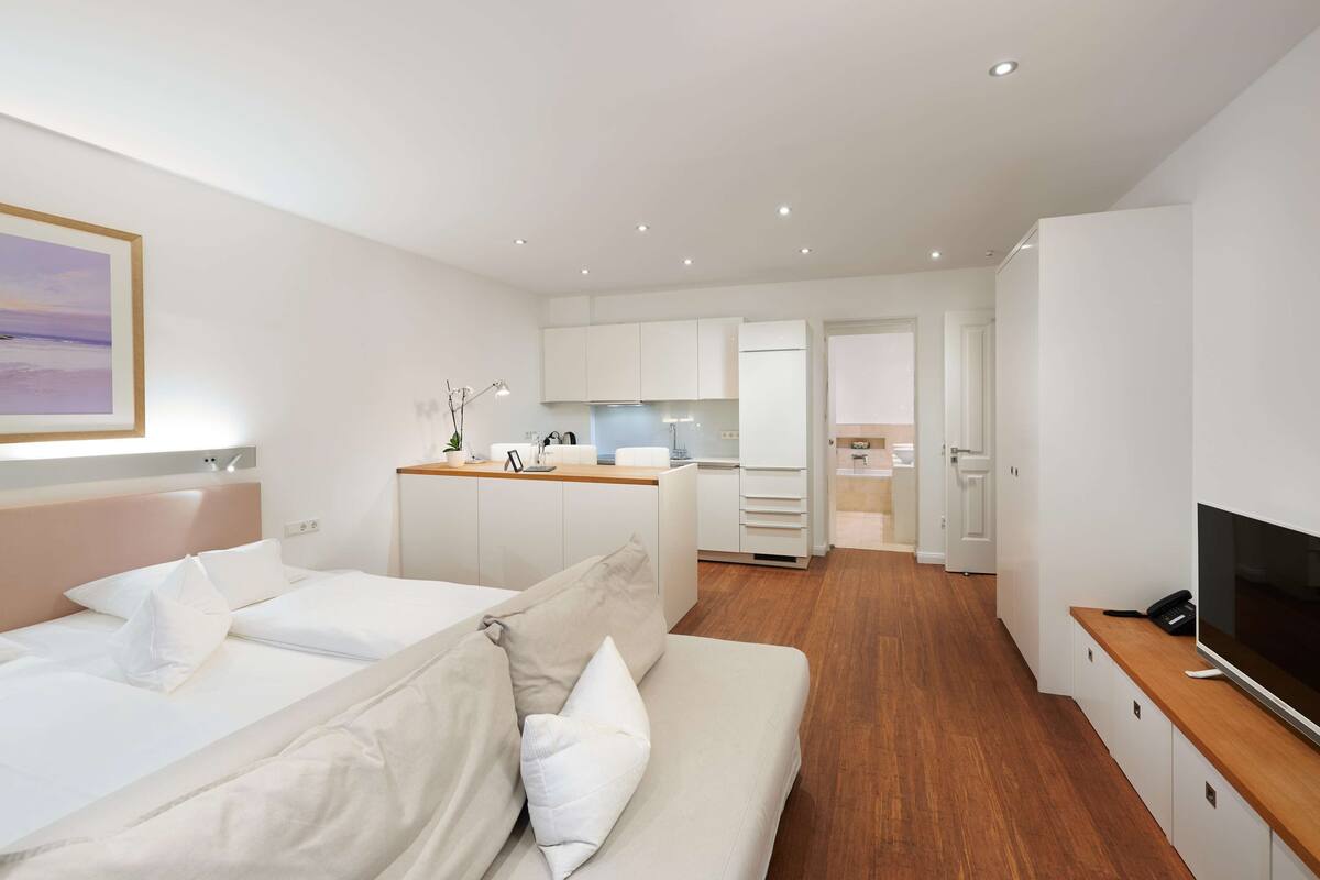 A modern hotel room with a bed, a sofa, a TV, and a kitchenette.