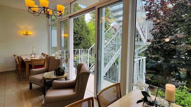Une pièce spacieuse dotée d’une grande fenêtre, d’un coin repas et d’un escalier menant à un espace extérieur.