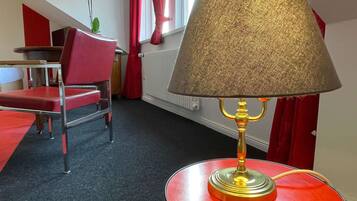 A room with a round table, a red chair, a lamp, and a radiator.