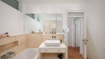 Un baño moderno con una bañera grande, un lavamanos blanco y un espejo con luz de aro.