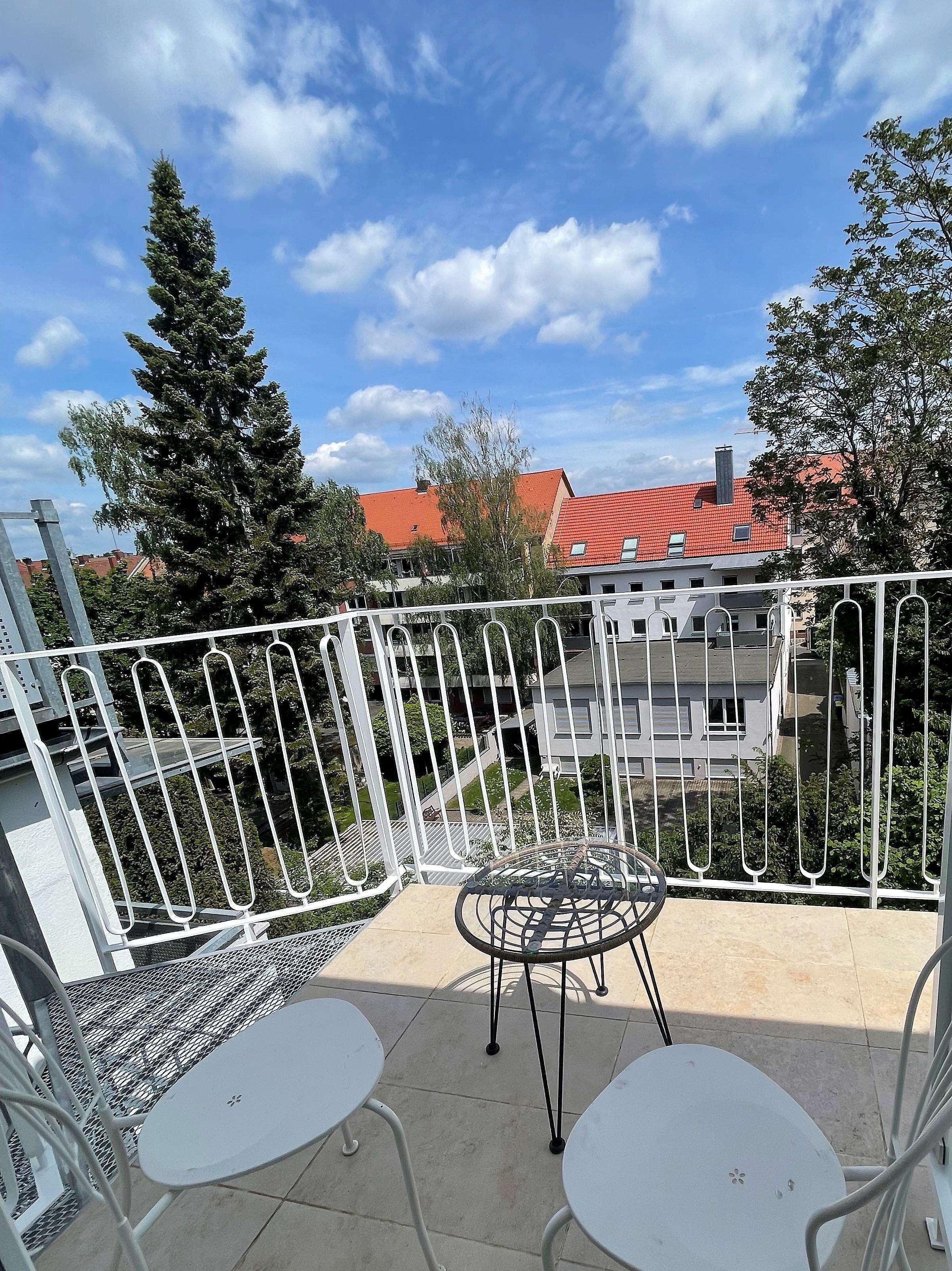 A balcony with two white metal tables and chairs, a metal railing, and a view of buildings with red roofs.