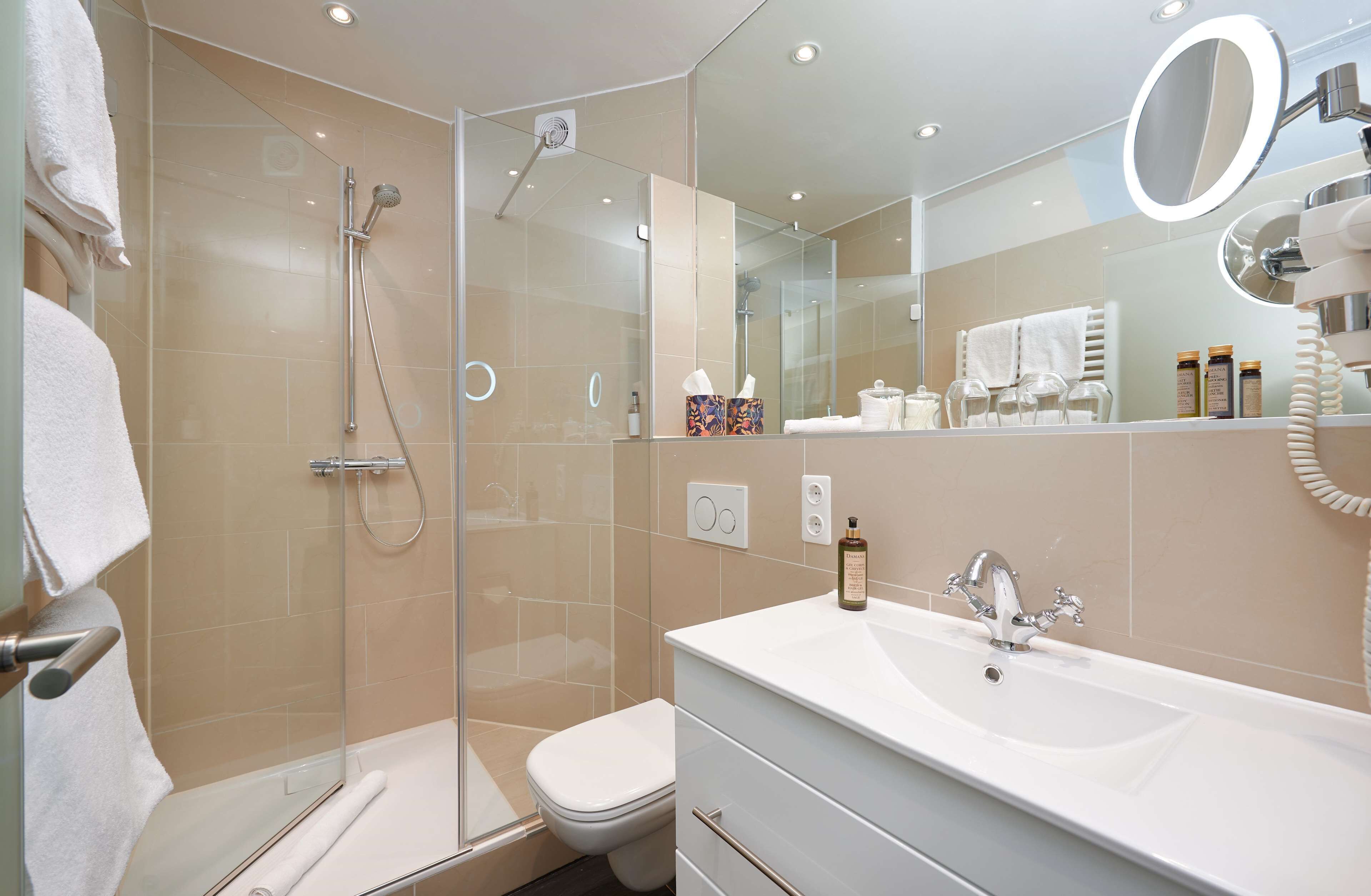 Ein modernes Badezimmer mit einer in Glas abgeschlossenen Dusche, einer weißen Toilette, einem großen Waschbecken und einem Spiegel mit rundem Waschtisch.