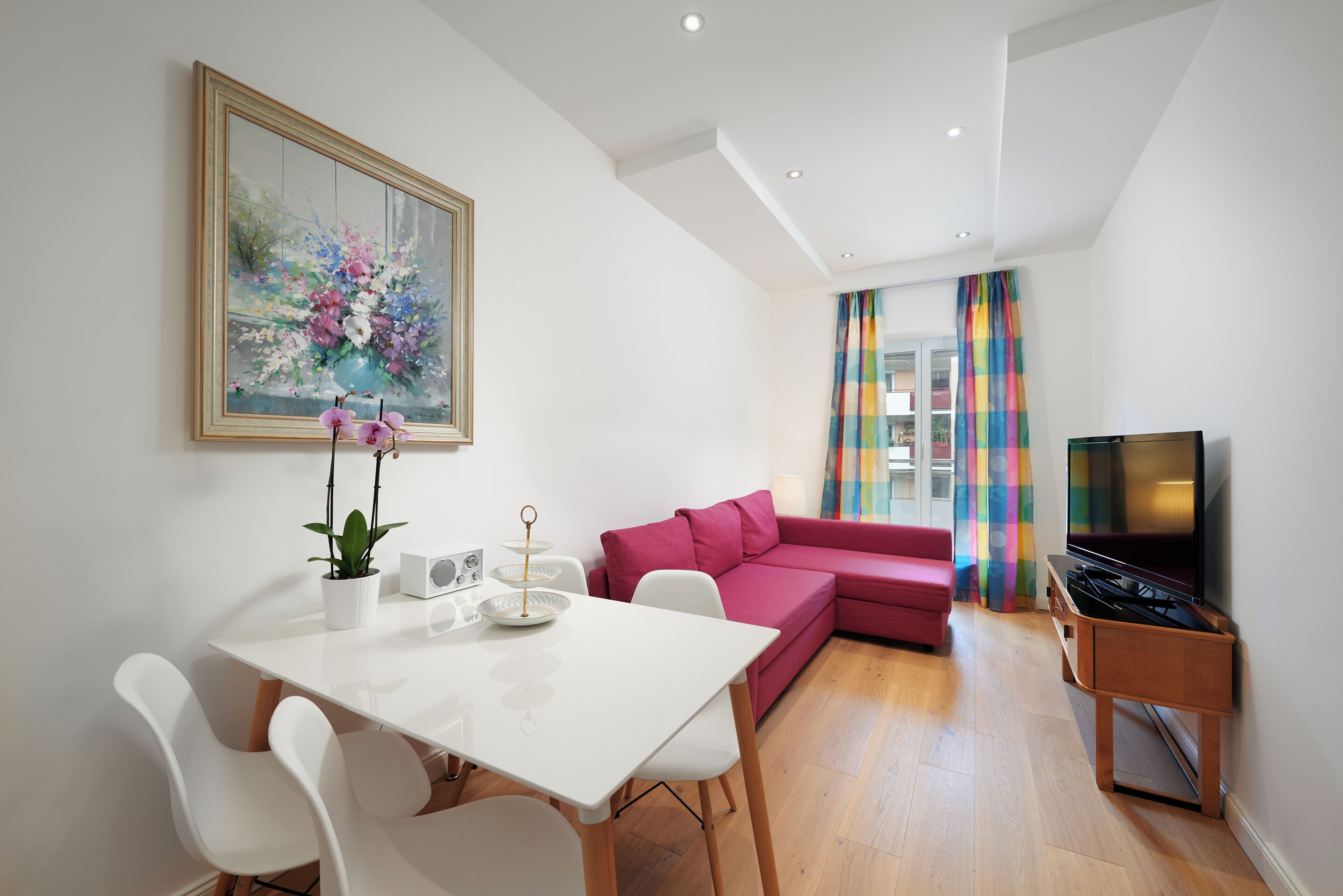 A modern living room with a white table, red sofa, and a TV stand.