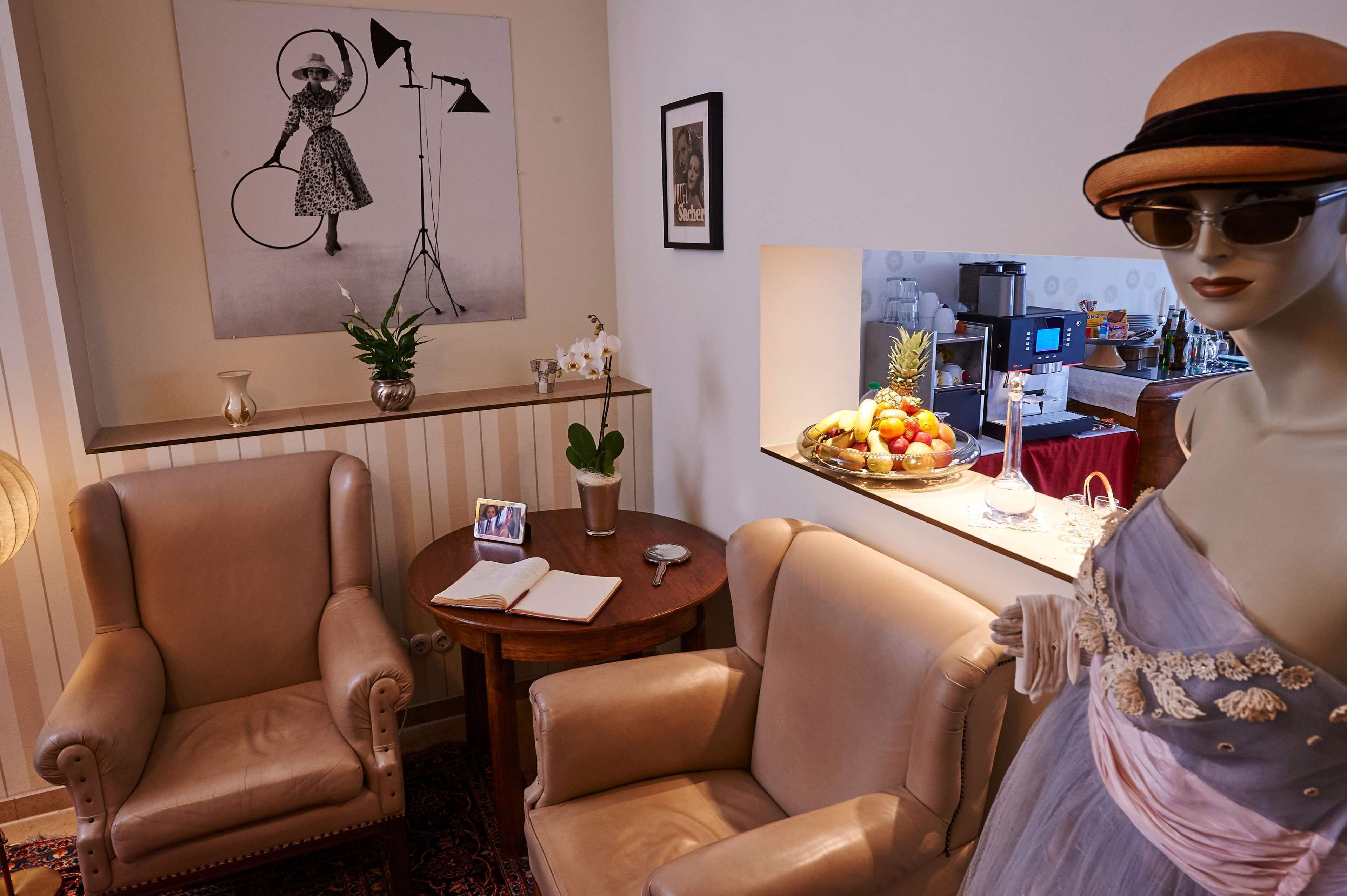 A room with two leather armchairs, a small round table with a vase and a book, a framed picture on the wall, and a mannequin dressed in a hat and dress.