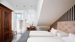 Une chambre à coucher avec un grand lit, une armoire en bois, un bureau avec une lampe et une vue sur l’extérieur.
