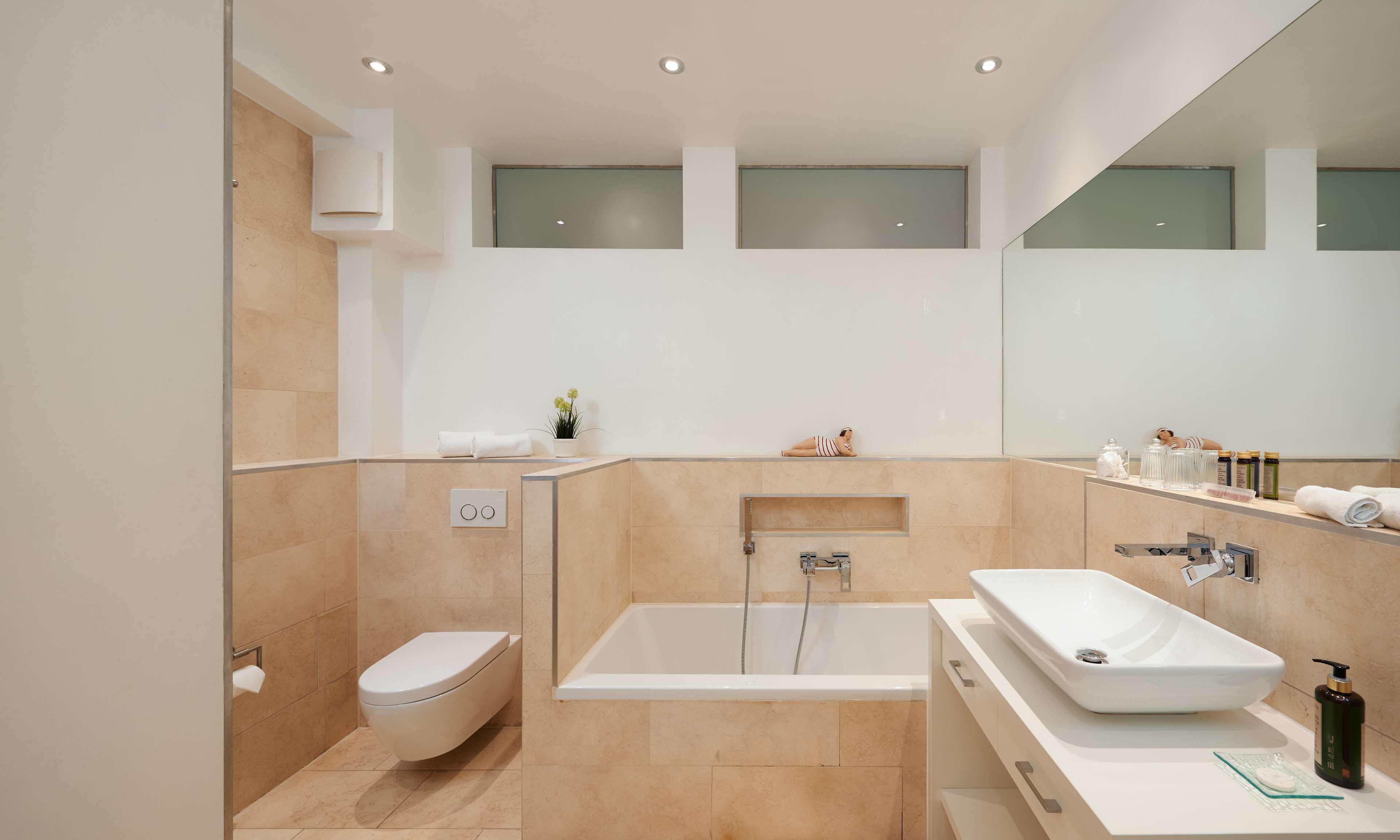 A modern bathroom with a toilet, bathtub, and a large mirror.