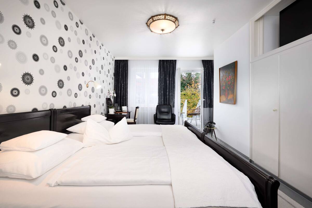 A hotel room with a large bed, a desk, a chair, and a view of the outdoors.