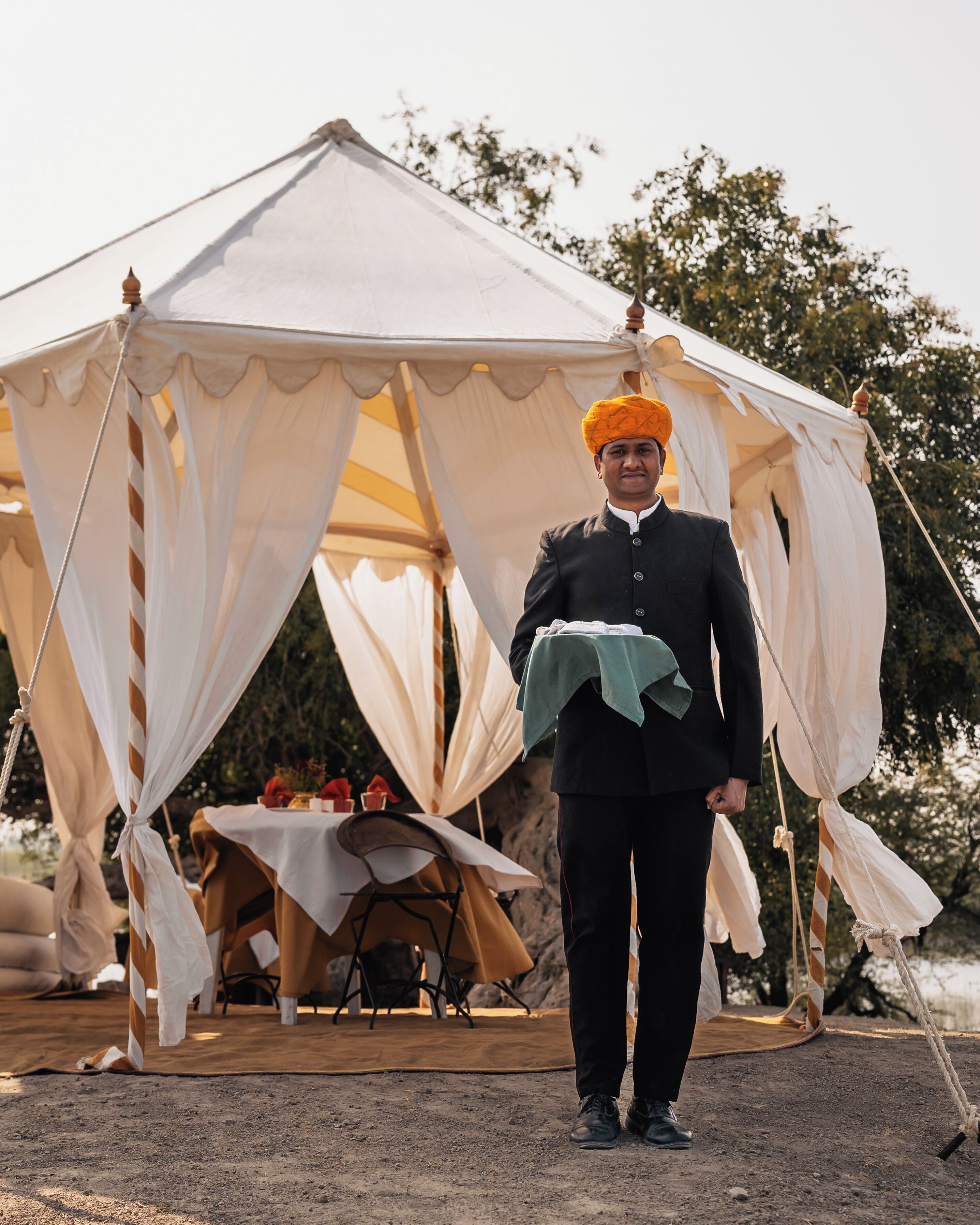 A tent with a table set up inside, a person standing in front of it, and a natural landscape in the background.