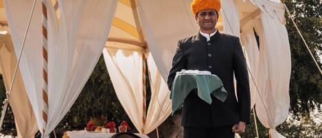 A tent with a table set up inside, a person standing in front of it, and a natural landscape in the background.